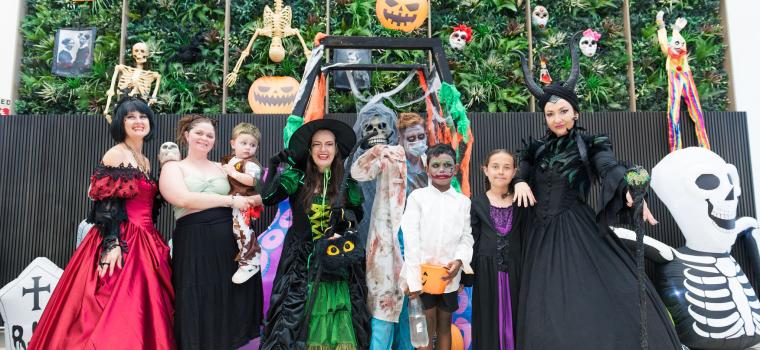 Community members and performers in Halloween costumes posing in front of a spooky Halloween display.